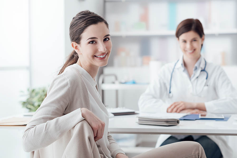 Smiling patient receiving a medical consultation and looking at camera, the female doctor is sitting at desk on the background