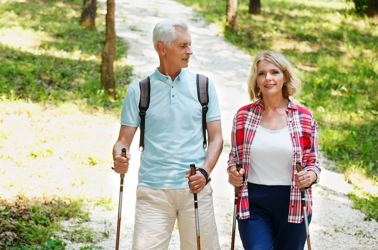 Portrait of senior couple enjoying a nordic walk. Active elderly woman and man walking on the forest and smiling.