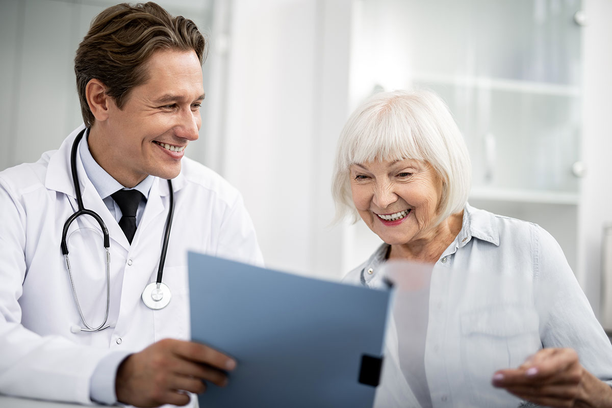 Positive practitioner smiling to his happy elderly patient while showing her positive results in personal folder