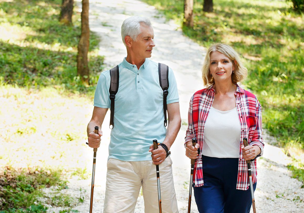 Portrait of senior couple enjoying a nordic walk. Active elderly woman and man walking on the forest and smiling.